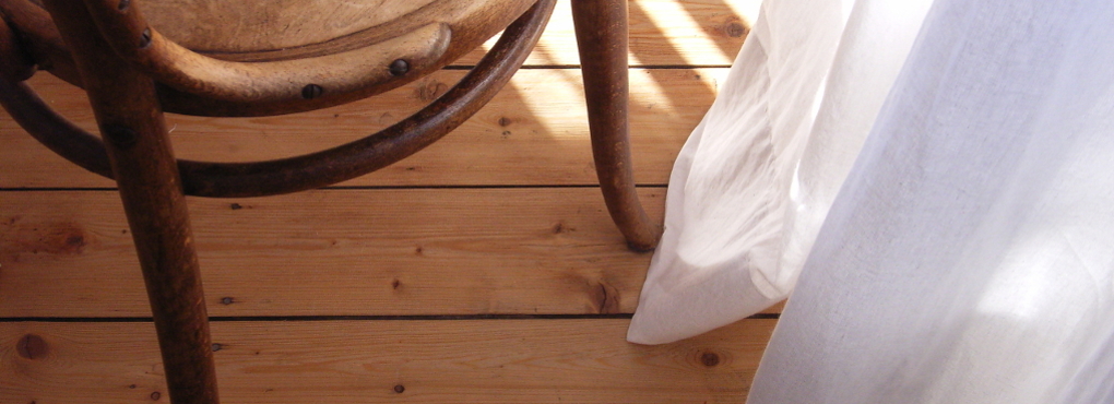 ausschnitt bugholzstuhl, holzfussboden und weisser Vorhang.